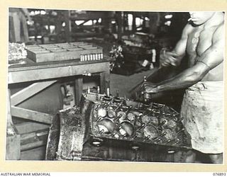 LAE, NEW GUINEA. 1944-11-15. AN AUSTRALIAN NEW GUINEA ADMINISTRATIVE UNIT NATIVE STRIPPING A FORD V8 MOTOR IN THE GENERAL ENGINEERING SECTION OF THE 2/7TH ADVANCED WORKSHOPS