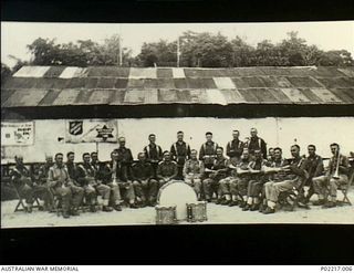 Jacquinot Bay, New Britain. 1945. Group portrait of musicians in the 36th Battalion, Australian Military Forces (AMF), band outside the hut shared by the Australian Comforts Fund (ACF) and ..