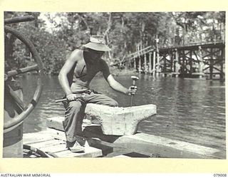 KALUMALAGI RIVER, NEW BRITAIN. 1945-02-12. N211015 SAPPER J.A. COLE, 17TH FIELD COMPANY, MAKING A WOODEN BOLLARD FOR THE WHARF SECTION OF THE NEW 30 TON BARGE SLIPWAY NEAR THE MOUTH OF THE RIVER