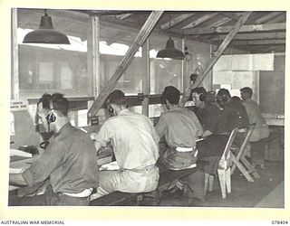 TOROKINA, BOUGAINVILLE ISLAND. 1945-01-18. THE INTERIOR OF THE SIGNALS OFFICE OF "B" CORPS OF SIGNALS SHOWING THE WIRELESS OPERATING BENCH. THE OPERATORS WEAR HEADPHONES WHICH ARE CONNECTED TO THE ..