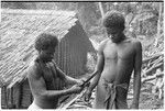 Man ties red cane obi on another man's wrist prior to a feast they are going to give