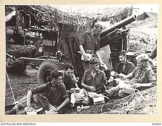 WEWAK AREA, NEW GUINEA, 1945-07-05. A GUN CREW OF A TROOP, 1 BATTERY, 2/1 FIELD REGIMENT, RECEIVING THEIR MID-YEAR AUSTRALIAN COMFORTS FUND HAMPERS WHILST STANDING TO IN THEIR GUN PITS AWAITING ..