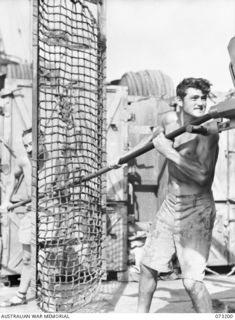 OFF MADANG, NEW GUINEA. 1944-05-14. ABLE SEAMAN A T LILLYE (AT THE BACGROUND) (1), ASSISTED BY ABLE SEAMAN E W CHURCHMAN (2), CLEAN THE 4 INCH NAVAL GUN ON THE STERN OF THE FRIGATE HMAS BARCOO. THE ..