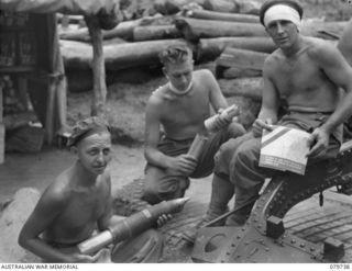 Pearl Ridge, Bougainville. 1945-03-09. SX24842 Gunner R. Warner (on left) loading the cardboard container which carries propaganda leaflets into a 25 pounder shell container. With him are VX70436 ..