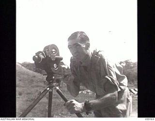 KILA, NEW GUINEA. 1943-10-24. VX117252 CAPTAIN G. H. NICHOLSON, OFFICER IN CHARGE, AUSTRALIAN MILITARY HISTORY SECTION, OPERATING A MOVIE CAMERA ON A TRIPOD