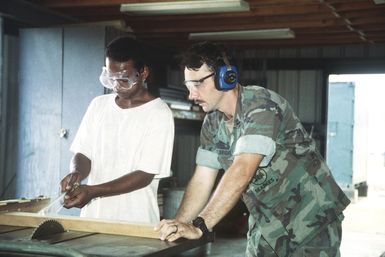 Equipment Operator Second Class (EO2) Larry Fulbright instructs a local worker of Palau in the basic functions of carpentry. After an apprenticeship of one year of training for the local work force, the Seabees hold an awards ceremony for the local residents who are then ready to join the local labor force