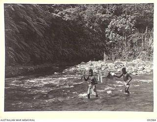 BOUGAINVILLE, 1945-05-31. NATIVE CARRIERS CROSSING THE HONGORAI RIVER ON THEIR WAY FROM NIHERO TO MORAKAIMORO WHERE THE 2/8 COMMANDO SQUADRON ARE OPERATING AGAINST THE JAPANESE