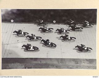 PALMALMAL PLANTATION, JACQUINOT BAY, NEW BRITAIN, 1945-07-05. WAX HORSES AND JOCKEYS OF THE NEW BRITAIN TURF CLUB PASS THE 7 FURLONG POST. THE MODELS ARE ON A RACE COURSE IN THE RECREATION HUT, 18 ..
