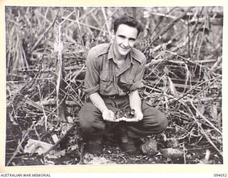 BOUGAINVILLE, 1945-07-16. GNR A.R. SMITH, 2 FIELD REGIMENT, HOLDING TWO WILD DUCKLINGS NEAR THE POOL CONSTRUCTED FOR THEM FROM A 25 POUNDER AMMUNITION BOX. THE DUCKLINGS WANDERED INTO 5 FIELD ..