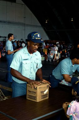 A master-at-arms inspects a family's luggage following their arrival at a temporary evacuation center during Operation Fiery Vigil. The center was set up to process military dependents who were evacuated from the Philippines after volcanic ash from the eruption of Mount Pinatubo disrupted operations at Clark Air Base and Naval Station, Subic Bay.