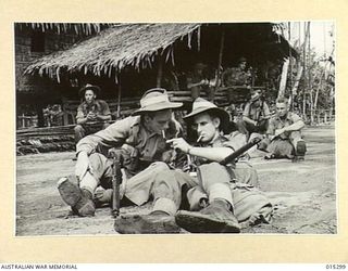 1943-07-28. NEW GUINEA. WARRANT OFFICER MICHAEL CURTIN OF MIDDLE PARK, VICTORIAM GIVES A LIGHT TO SGT. FRANK MADDEN OF SOUTH BRISBANE, AS AUSTRALIAN TROOPS REST IN A DESERTED NATIVE VILLAGE IN THE ..