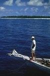 Standing on the bow of a boat is a Samoan native, as photographed by a member of the Capricorn Expedition (1952-1953) during a stopover in American Samoa. 1953