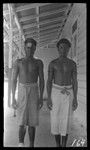 Two men outside a building, one with forehead marking