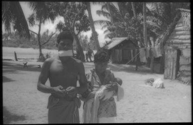 Man and woman holding a baby with house in background : Carteret Islands, Papua New Guinea, 1960 / Terence and Margaret Spencer