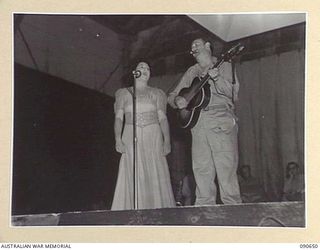 TOROKINA, BOUGAINVILLE. 1945-04-14. WILLA HOKIN (1), AND BOB DYER (2), MEMBERS OF THE BOB DYER CONCERT PARTY SING "WALTZING MATILDA" AS A DUET TO ENTERTAIN TROOPS AT BOSELY FIELD