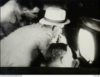 IN FLIGHT BETWEEN HOLLANDIA, DUTCH NEW GUINEA AND AITAPE, NORTH EAST NEW GUINEA. C. 1944-06. ARTHUR DRAKEFORD (STANDING, WEARING PANAMA HAT), THE MINISTER FOR AIR, LOOKING THROUGH THE WINDOW OF THE ..