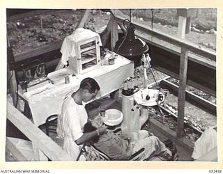 LAE AREA, NEW GUINEA. 1945-05-25. MAJOR L.P. SKUES, 54 DENTAL UNIT (1), OPERATING IN HIS SURGERY. THE PHOTOGRAPH INDICATES LIGHTING SYSTEM AND VENTILATION