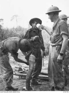 Temporary treatment is given to walking wounded Australian, who has just come in from the front line. Corporal George Wilson, 2/12th Battalion gives the wounded soldier a drink