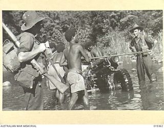 1943-07-31. ALLIED CAPTURE OF MUBO. MANHANDLING AN AMERICAN ARTILLERY PIECE ACROSS A CREEK NEAR NASSAU BAY. THE GUNS WERE HAULED THROUGH COUNTRY THAT WAS ALMOST IMPASSABLE. NATIVES IN ADDITION TO ..