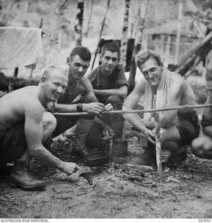 PAPUA, NEW GUINEA, 1942-10. PERSONNEL OF THE AIR SUPPORT CONTROL SIGNALS COOKING THEIR TEA BY A SMALL FIRE IN THE JUNGLE AT NAURO, IN THE OWEN STANLEYS REGION. THE MAN ON THE RIGHT IS CORPORAL J. ..
