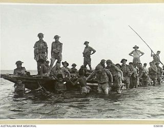 PAPUA, NEW GUINEA. 1942-07. AN AUSTRALIAN INFANTRY PATROL BEING TRANSPORTED ACROSS A RIVER BY SMALL BOYS IN A "LAKATOI" GET OFF AND PUSH ACROSS THE SHALLOW WATERS OVER THE REEF WHICH GIRDLES THE ..