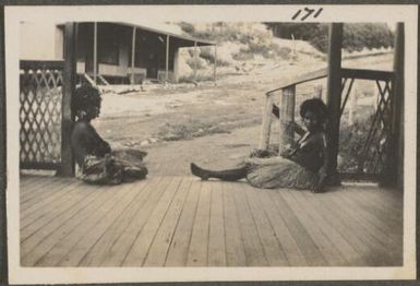 Two girls wearing grass skirts, on a verandah, Port Moresby, Papua New Guinea, probably 1916