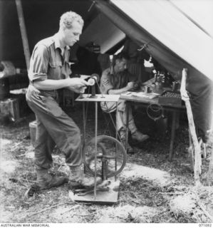 KILIGIA, NEW GUINEA. 1944-03-13. NX10836 CORPORAL F.P. MCGRATH (1), A DENTAL MECHANIC OF "E" SECTION, 2/5TH DENTAL UNIT, GRINDS A SET OF DENTURES ON A PORTABLE PEDAL OPERATED LATHE IMPROVISED BY ..