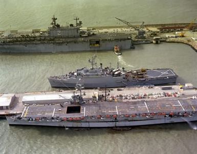 An aerial view of ships anchored. The ships are, from front to back, the Spanish ship DEDALO (PA-01), the amphibious transport dock USS RALEIGH (LPD-1)and the amphibious assault ship USS SAIPAN (LHA-2)