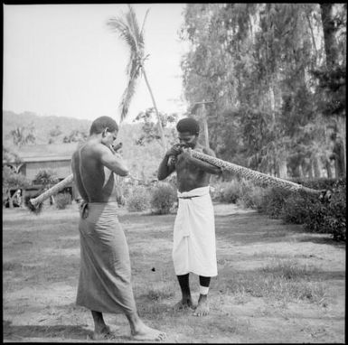 Two men blowing long decorated trumpets, New Guinea, ca. 1936 / Sarah Chinnery