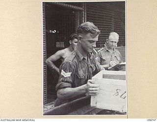 BORAM, NEW GUINEA. 1945-11-16. CORPORAL N.T. MAYOH (1) AND STAFF SERGEANT W.R. SEACH (2); MEMBERS OF 3 BASE SUB AREA, AUSTRALIAN ARMY CANTEENS SERVICE, CHECKING AND LOADING CANTEEN SUPPLIES ONTO A ..