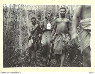 WAITAVALO AREA, WIDE BAY, NEW BRITAIN. 1945-03-16. AUSTRALIAN NEW GUINEA ADMINISTRATIVE UNIT NATIVES ASSIST WOUNDED OF HEADQUARTERS 6TH INFANTRY BRIGADE FROM THE RIDGES BEHIND WAITAVALO AND TOL ..
