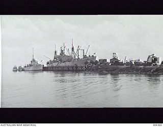 LORENGAU, ADMIRALTY ISLANDS. 1947-07. NABU WHARF, LOOKING SEAWARDS. THE APPROACH TO THE WHARF IS LITTERED WITH A VARIETY OF CONSTRUCTION EQUIPMENT. ALONGSIDE IS THE ATTACK TRANSPORT USS LEO ..