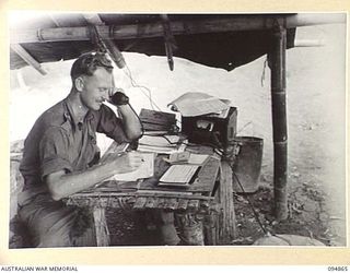 YAMIL 2, NEW GUINEA. 1945-08-01. LIEUTENANT J.E. MASON, REGIMENTAL QUARTERMASTER, 2/6 INFANTRY BATTALION, AT WORK. HIS JOB DEALS DAILY WITH DETACHING NATIVES WHO ARE ATTACHED TO THE BATTALION FROM ..