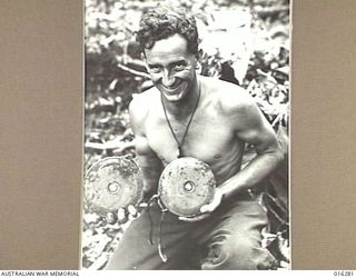 NEW GUINEA. 17 DECEMBER 1943. CPL. A.B. RUTLEDGE OF BERRY, N.S.W. HOLDING TWO OF MANY JAPANESE LAND MINES WHICH WERE DUG UP BEFORE ANY DAMAGE WAS CAUSED IN THE VICINITY OF GUSIKA. THIS AREA WAS ..