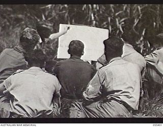 WAU, NEW GUINEA. 1943-08-9-12. WARRANT OFFICER J. H. WINSTANLEY OF THE AUSTRALIAN ARMY EDUCATION SERVICE, CONDUCTING A CLASS IN MUSICAL THEORY, WITH THE AID OF A CHART