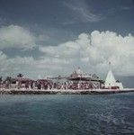 People at a French Polynesian pier with a sign reading "Bienvenue M. et Mme. Le Goveneur"