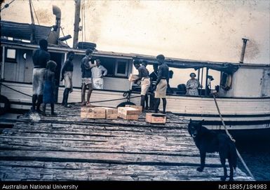 Group of dockworkers unloading boat, dog in foreground