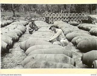 1943-06-25. NEW GUINEA. LIEUT. WILLIAM MOREAU, OF NEW JERSEY, AND TECH SERGEANT JOHN D. MILLS, OF MONROE, NORTH. CAROLINA, CHECKING OVER 1,000 AND 2,000 POUND BOMBS. THESE BOMBS ARE WAITING TO GO ..