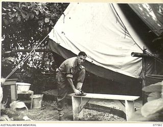 SX23539 WARRANT OFFICER II, G.J. TELFER, REGIMENTAL QUARTERMASTER SERGEANT, NO. 6 PLATOON, HEADQUARTERS COMPANY, 27TH INFANTRY BATTALION POLISHING HIS BOOTS OUTSIDE HIS TENT