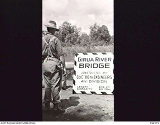 LOPUTA, NEW GUINEA, 1943-07-20. N297807 PRIVATE H. E. WRIGHT OF 11TH AUSTRALIAN DIVISION PROV COMPANY READS THE SIGN ERECTED BY C.O. "C" 116TH ENGINEERS, 41ST DIVISION, THE AMERICAN UNIT WHICH ..