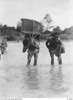 A native carrier with the 35th Infantry Battalion carries an abandoned Japanese armchair across the river during the unit's advance along the coast towards Wewak