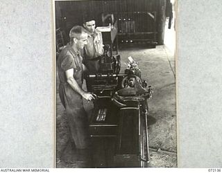 PORT MORESBY, NEW GUINEA. 1944-04-10. NX48162 CORPORAL A.M. SUMMERS (1), WATCHED BY WX4553 LIEUTENANT W.E. SMITH (2), GRINDS A JEEP CRANK SHAFT AT THE 11TH ADVANCED WORKSHOP, AUSTRALIAN ELECTRICAL ..