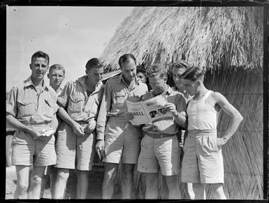 Portrait of unidentified RNZAF personnel with their latest mail in hand, reading Whites Aviation magazine in front of a thatched hut at [Fua'Amotu?] Airfield, Tonga