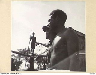 CAPE PUS, NEW GUINEA. 1945-09-29. CAPTAIN F.G. BELL, 2/3 INFANTRY BATTALION, TELLING A NATIVE THE WORK WANTED ON THE BUILDING. THE NATIVES DO MOST OF THE BUILDING AROUND THE CAMP