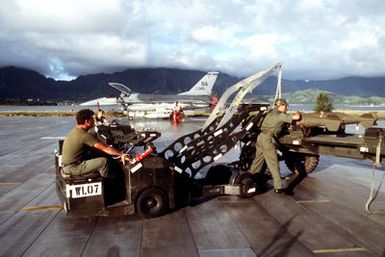 Airmen use a bomb loader to remove one of the Mark 82 500-pound laser-guided bombs from a munitions cart during exercise COPE ELITE '81. The F-16 Fighting Falcon aircraft (in the background) which will carry the bombs is from 428th Tactical Fighter Squadron, 474th Tactical Fighter Wing