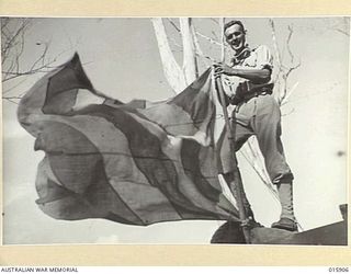 1943-10-02. NEW GUINEA. NADZAB AERODROME. LIEUT J. SANDELL FO MIDDLE PARK, VICTORIAN, WITH THE LANDING FLAG THE JAPANESE USED AT NADZAB AIRSTRIP. THE FLAG IS NOW USED TO SIGNAL OUR PLANES. ..