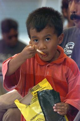 A little boy has a Humanitarian Meal Ready to Eat (MRE) for a late lunch as his family waits for a room assignment at the temporary housing in converted dorms at Andersen Air Force Base south, Guam, after Super Typhoon Paka destroyed or badly damaged their homes