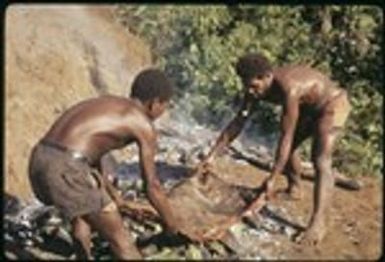 Two men laying pork out on the stone oven