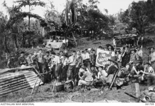 WAREO, NEW GUINEA. 1943-12-09. AS THE FLAG OF THE 2/23RD AUSTRALIAN INFANTRY BATTALION WAS BEING HOISTED, A SALVATION ARMY OFFICER WAS PUTTING UP HIS SIGN, AFTER HAVING FOLLOWED THE BATTALION RIGHT ..