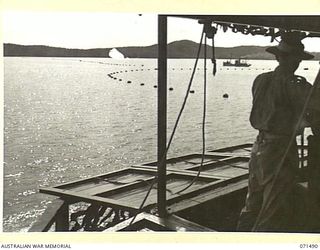 PORT MORESBY, PAPUA, NEW GUINEA. 1944-03-27. A SERGEANT PICTURED CLEANING THE ANTI-AIRCRAFT SEARCHLIGHT AT A CAMOUFLAGED COMMAND POST AT PAGA BATTERY, COAST ARTILLERY, OVERLOOKING THE ..